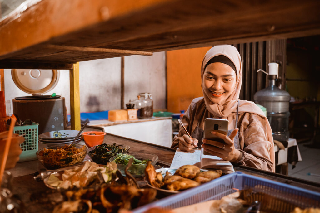 Ide Jualan Ramadhan untuk UMKM. Perempuan hijab bisnis makanan dengan pencatatan keuangan.